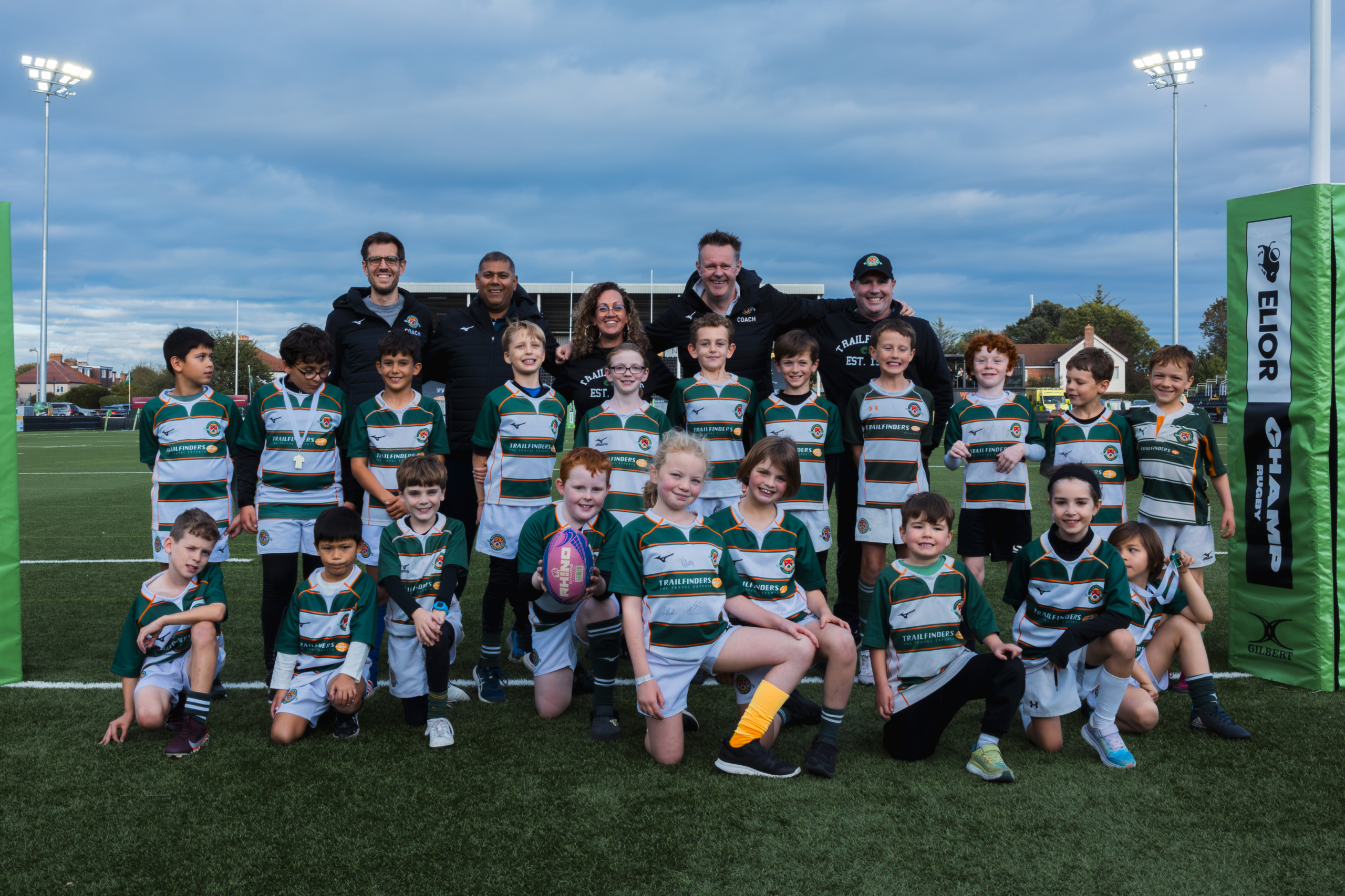 Festival rugby team and coaches pose under the posts on the main pitch at Trailfinders Sports Club